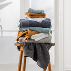 Stack of Egyptian cotton face cloths in assorted colours displayed on a wooden stool in a bright bathroom setting.