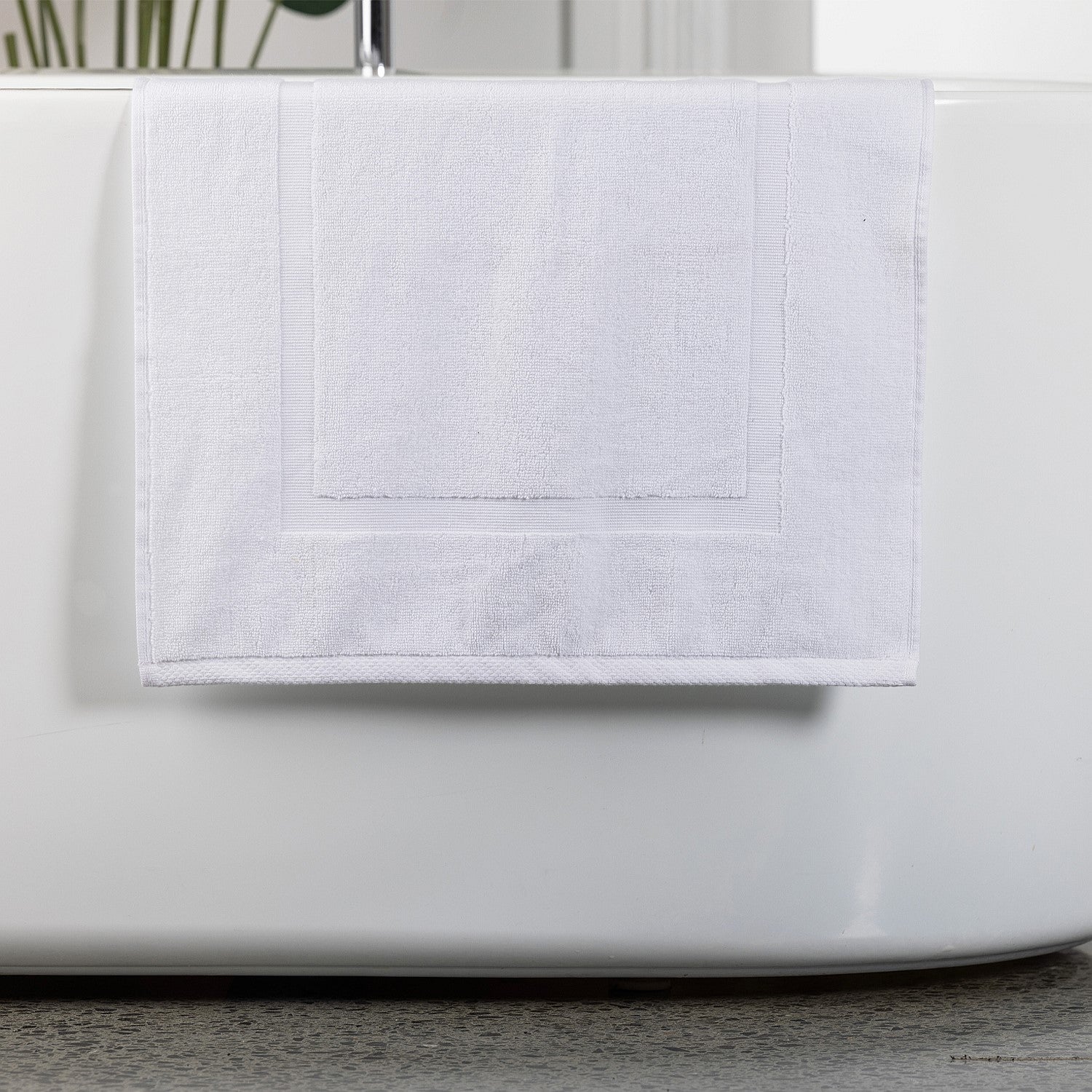 White bath mat hanging over bath tub