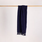 Navy blue throw with fringes hanging on a wooden rod against a light gray background