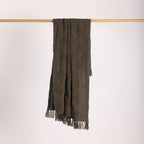 Green woven throw with fringes on a wooden rod against a white background