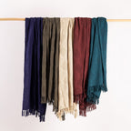 Five throws in different colors hanging on a wooden rod against a white background