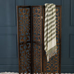 Decorative wooden screen with a striped throw against a dark blue wall