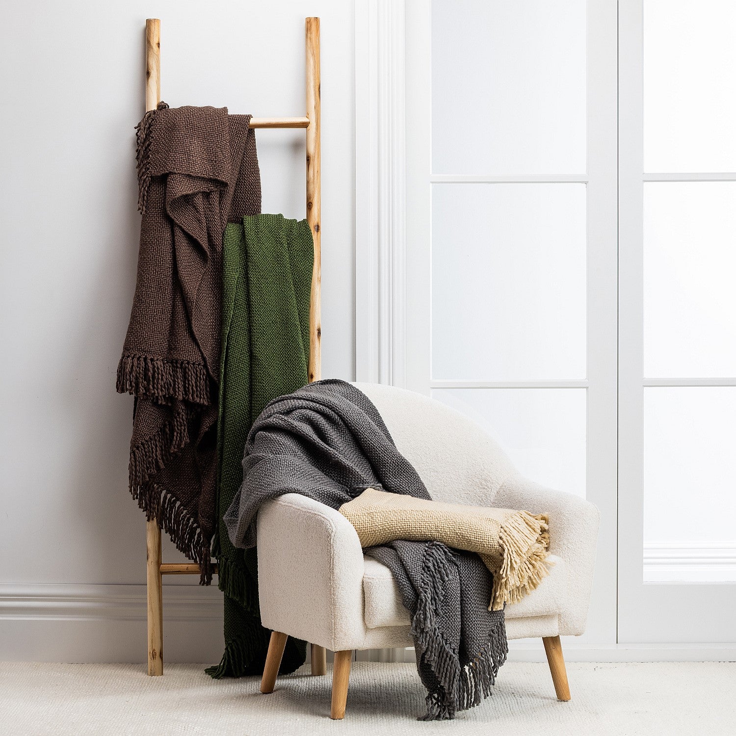 Wooden ladder with throws draped over it against a white wall.