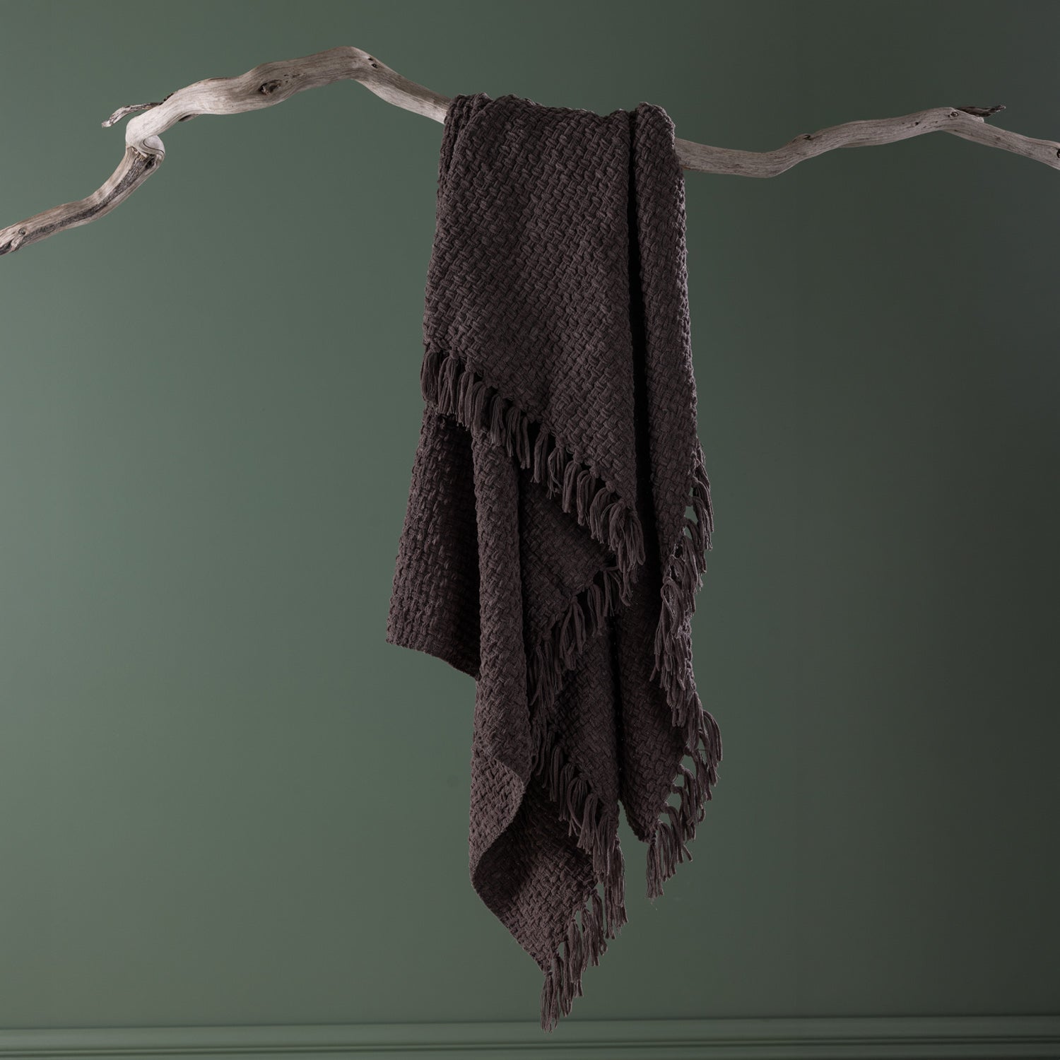 Home Co. Tilly Throw in Charcoal draped over a natural driftwood branch, showcasing the textured woven finish and tassel edging.