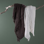 Home Co. Tilly Throws in Charcoal and White draped over a natural driftwood branch, showcasing the textured woven design and decorative tassel fringe.