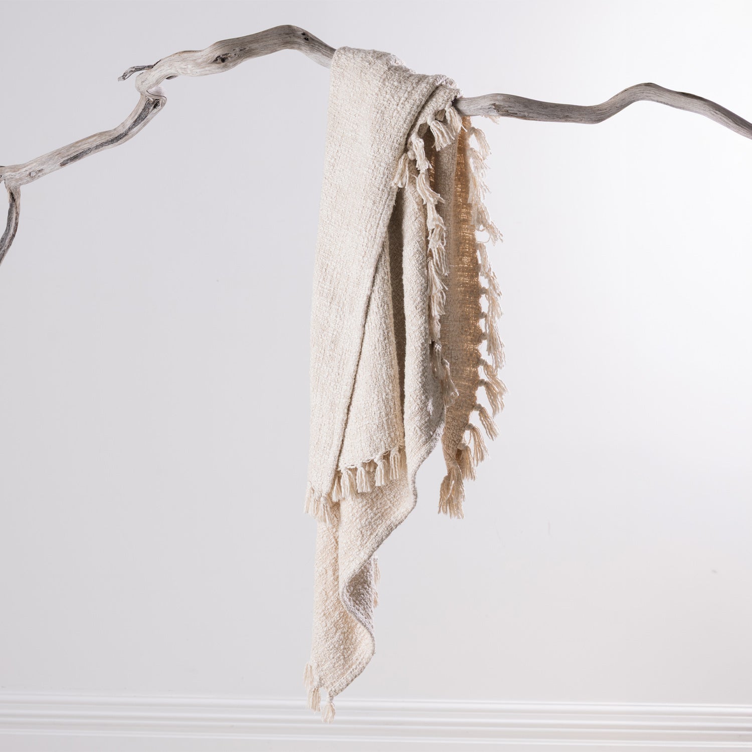 Home Co. Mateo Throw in Natural draped over a natural driftwood branch, highlighting the textured weave and tassel detail.