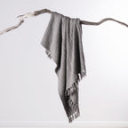 Home Co. Mateo Throw in Silver draped over a natural driftwood branch, featuring a textured woven finish with tassel edging.