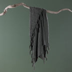 Sage green textured throw blanket with tassel fringe draped over a natural driftwood branch against a soft sage green background.