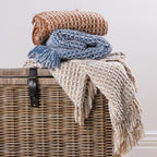A coordinated stack of textured woven fringed throws in warm rust, natural, and blue tones creates a cosy and inviting home décor display.