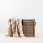Natural throw blanket draped over a woven storage basket with a white background 