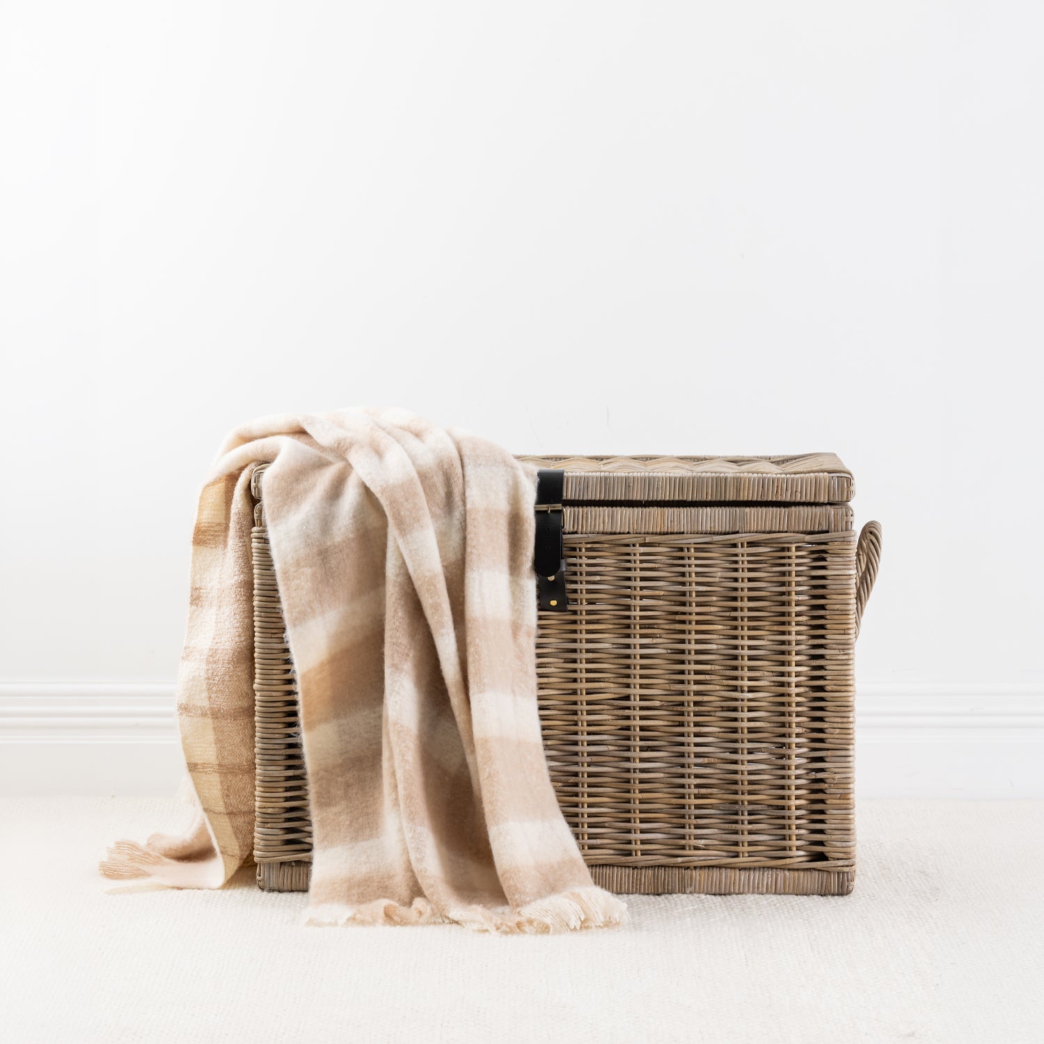 Natural throw blanket draped over a woven storage basket with a white background 