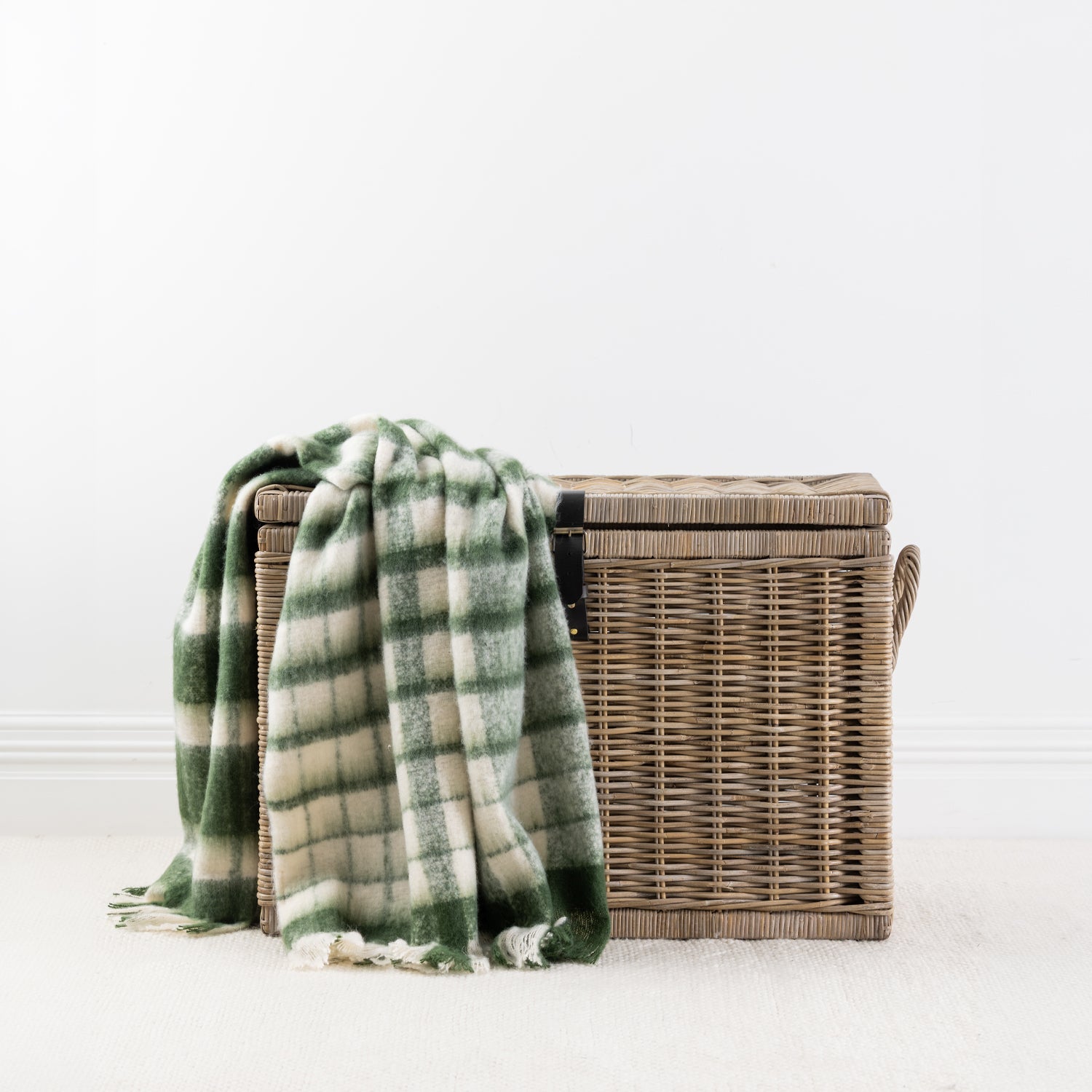 Olive throw blanket draped over a woven storage basket with a white background 