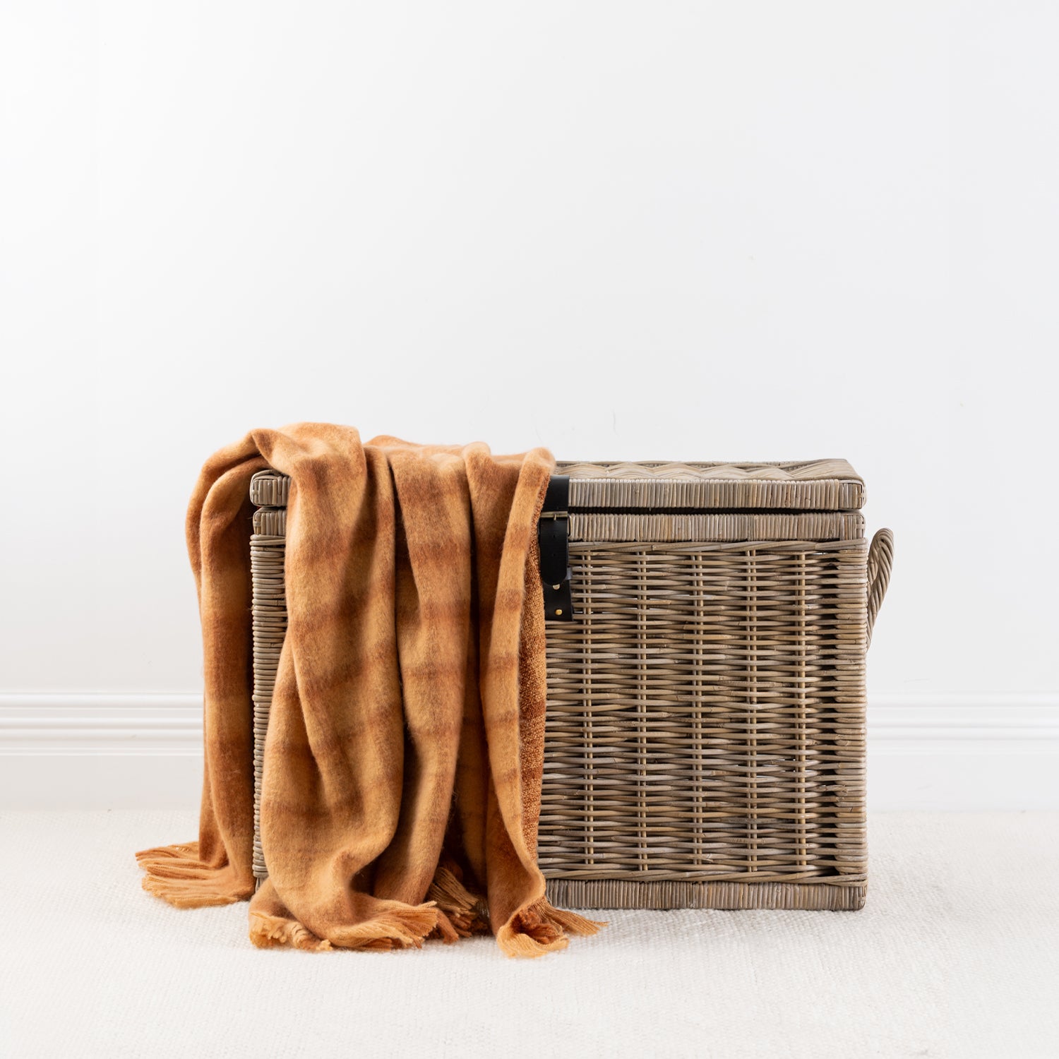 Rust throw blanket draped over a woven storage basket with a white background 