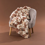 Amparo Macey Throw in blush draped over a grey chair, featuring a soft faux fur spotted design.