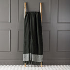 Olive New Zealand wool throw draped over a wooden ladder against a grey panelled wall.