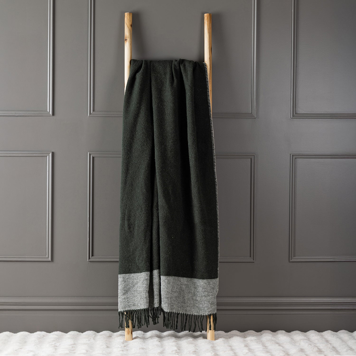 Olive New Zealand wool throw draped over a wooden ladder against a grey panelled wall.