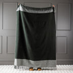 Olive New Zealand wool throw held up against a grey panelled wall.