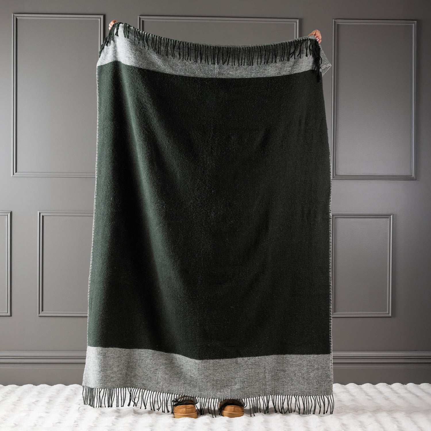 Olive New Zealand wool throw held up against a grey panelled wall.