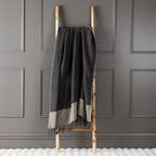Charcoal New Zealand wool throw draped over a wooden ladder against a grey panelled wall.