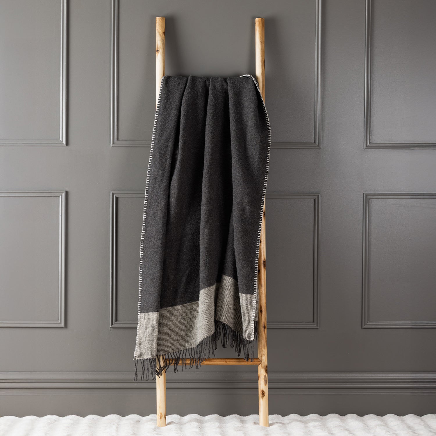 Charcoal New Zealand wool throw draped over a wooden ladder against a grey panelled wall.