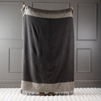 Charcoal New Zealand wool throw held up against a grey panelled wall.