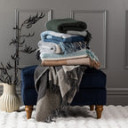 Stack of New Zealand wool throws in assorted colours styled on a navy ottoman with a decorative vase.