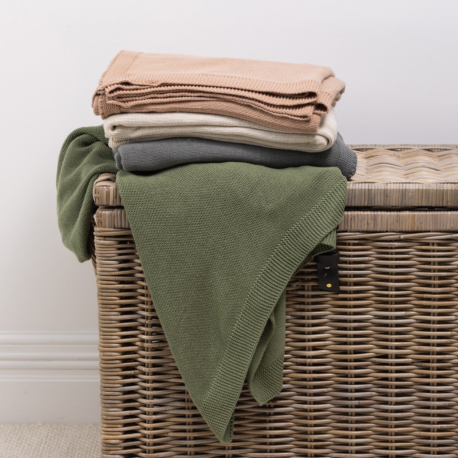 A collection of knitted cotton throws in soft, versatile colours is neatly folded and styled over a woven wicker storage trunk, bringing warmth, texture and effortless style to any living space.