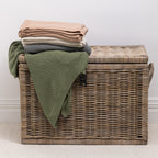 A collection of knitted cotton throws in soft, versatile colours is neatly folded and styled over a woven wicker storage trunk, bringing warmth, texture and effortless style to any living space.