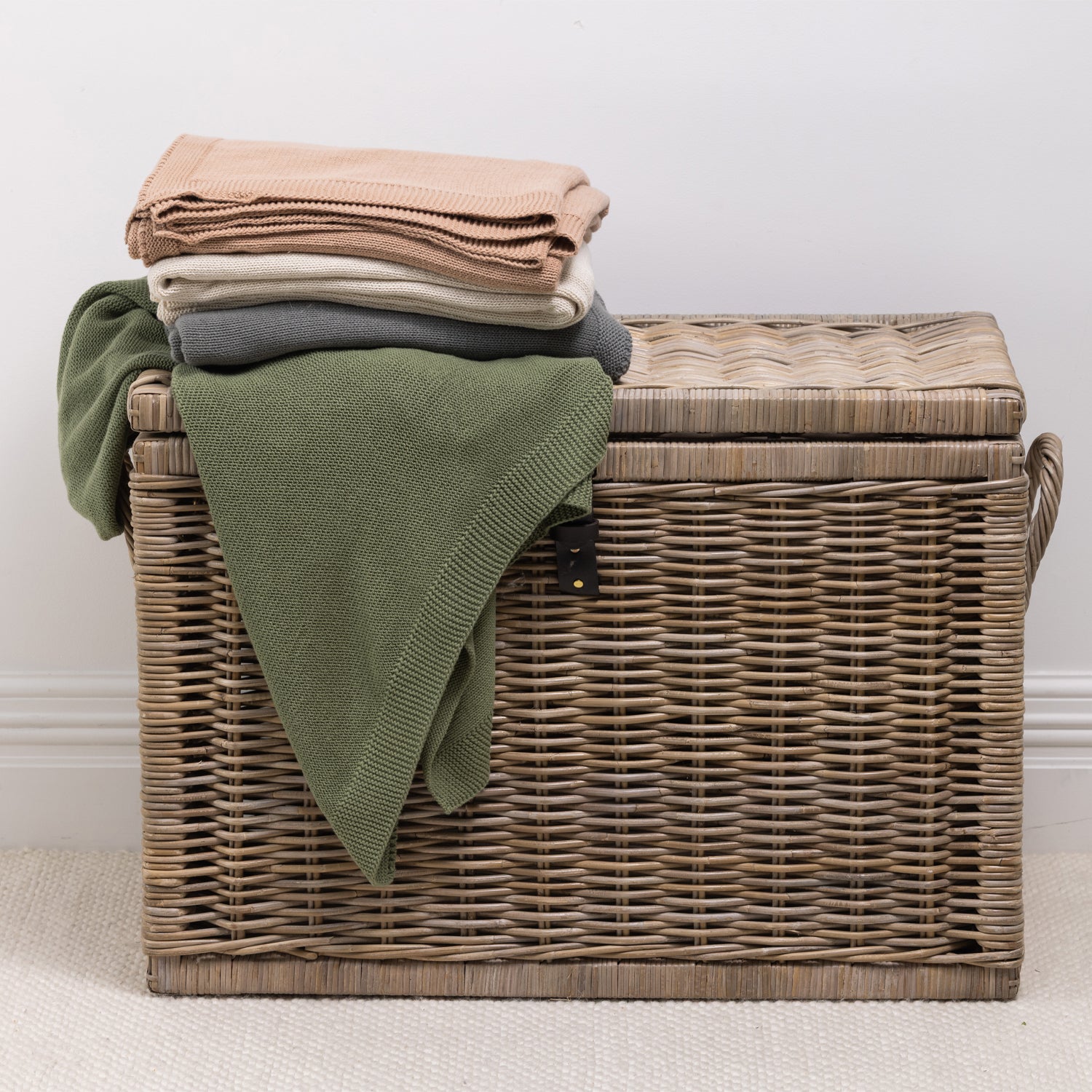 A collection of knitted cotton throws in soft, versatile colours is neatly folded and styled over a woven wicker storage trunk, bringing warmth, texture and effortless style to any living space.