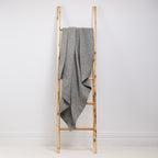 A textured cotton waffle throw is draped over a wooden ladder.