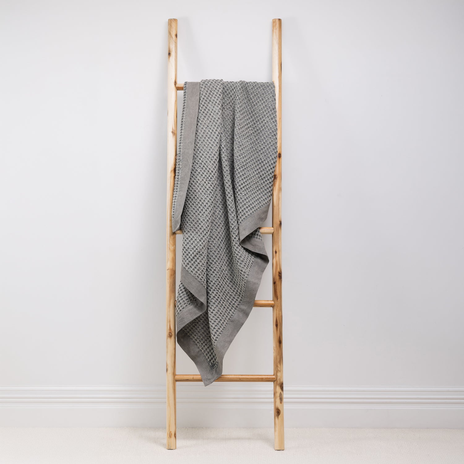 A textured cotton waffle throw is draped over a wooden ladder.