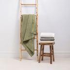 A textured cotton waffle throw is draped over a wooden ladder alongside neatly folded coordinating throws, showcasing its timeless design and effortless layering appeal.