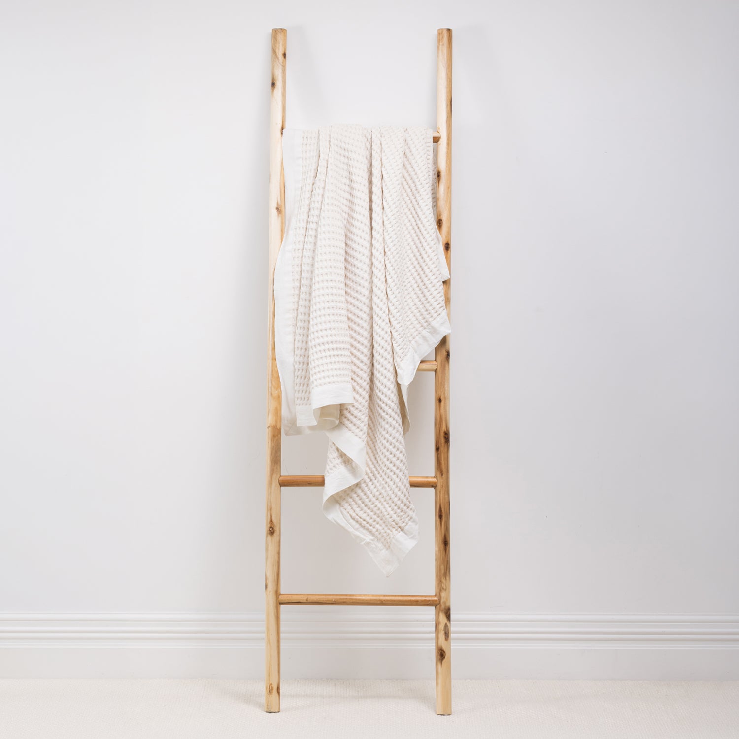A textured cotton waffle throw is draped over a wooden ladder.