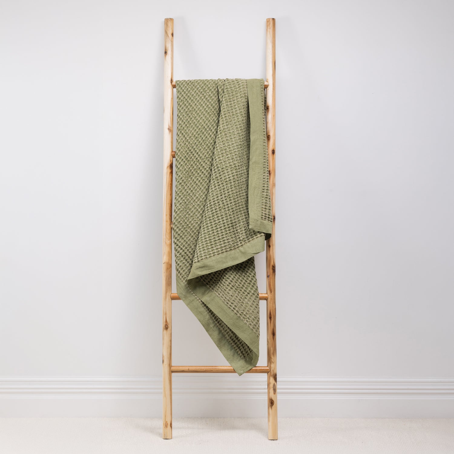 A textured cotton waffle throw is draped over a wooden ladder.