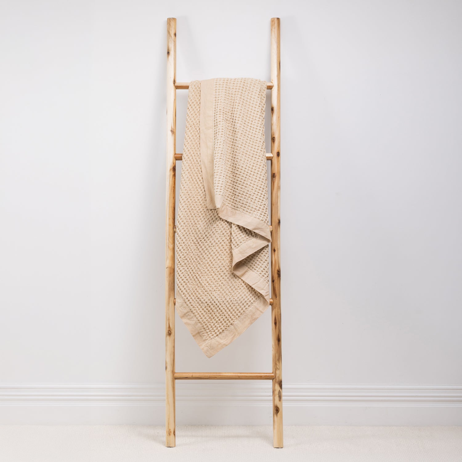 A textured cotton waffle throw is draped over a wooden ladder.