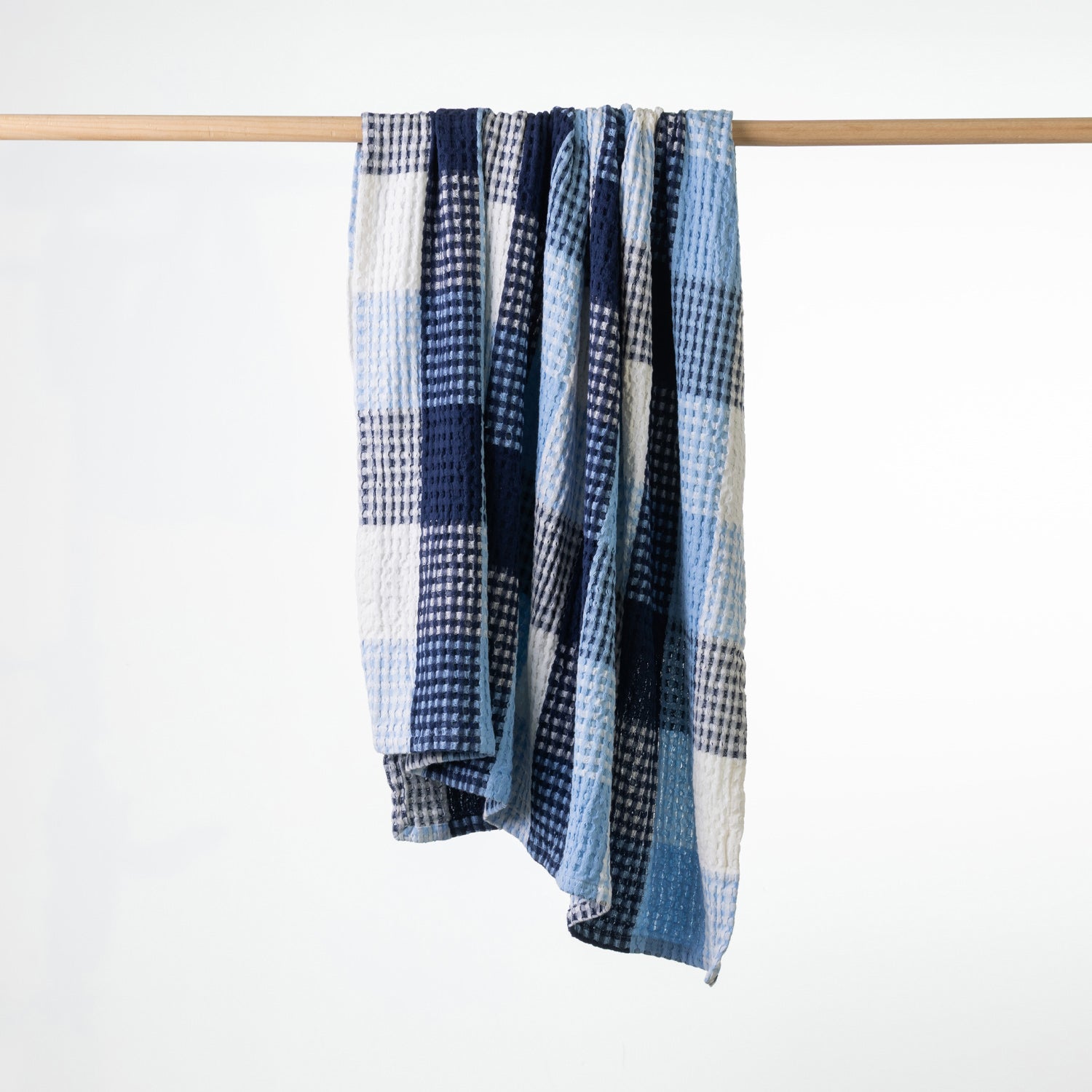 A blue checkered waffle throw draped over a light wood hanging rod against a plain white background.