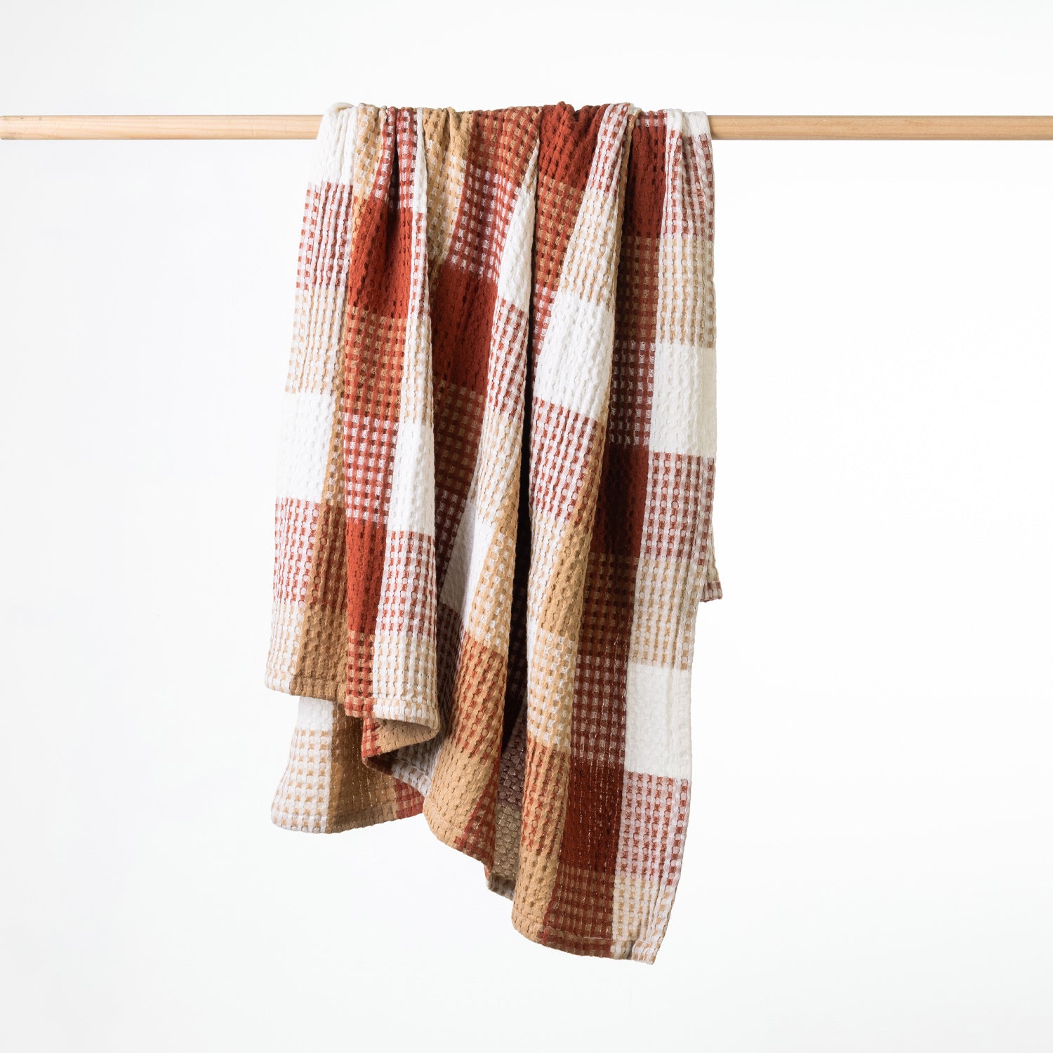 A textured waffle throw with a warm rust plaid pattern, hanging from a light wood rod against a clean white background.
