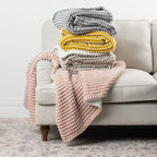 Home Co. Aiden Throw range in Pink, Natural, Mustard and Silver, displayed together on a neutral sofa.
