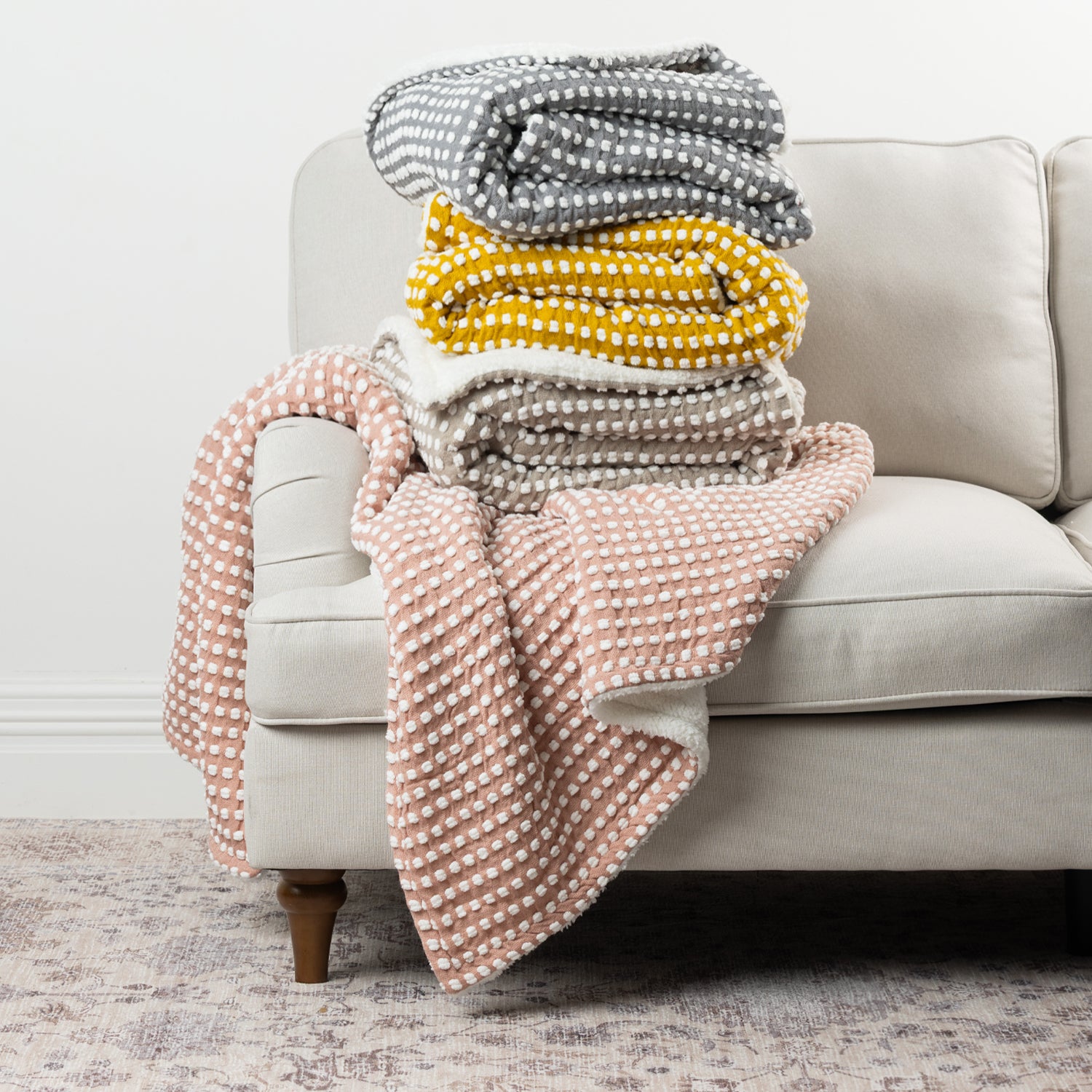 Home Co. Aiden Throw range in Pink, Natural, Mustard and Silver, displayed together on a neutral sofa.