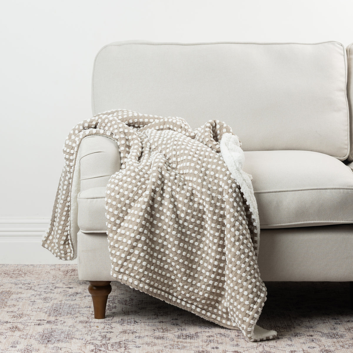 Home Co. Aiden Throw in Natural featuring a raised white dot pattern and soft sherpa reverse, draped over a neutral sofa.
