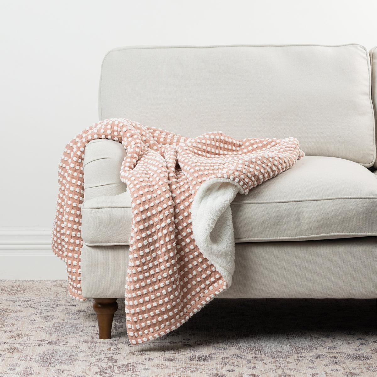 Home Co. Aiden Throw in Pink featuring a raised white dot pattern and soft sherpa reverse, styled over a neutral sofa.