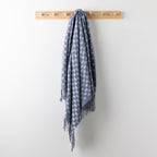 Home Co. Solane Check Throw in Blue featuring a blue check pattern and fringed edges, hanging from a wooden wall rack.