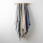 Home Co. Solane Check Throw range in Silver, Sage, Natural and Blue, displayed together on a wooden wall rack.