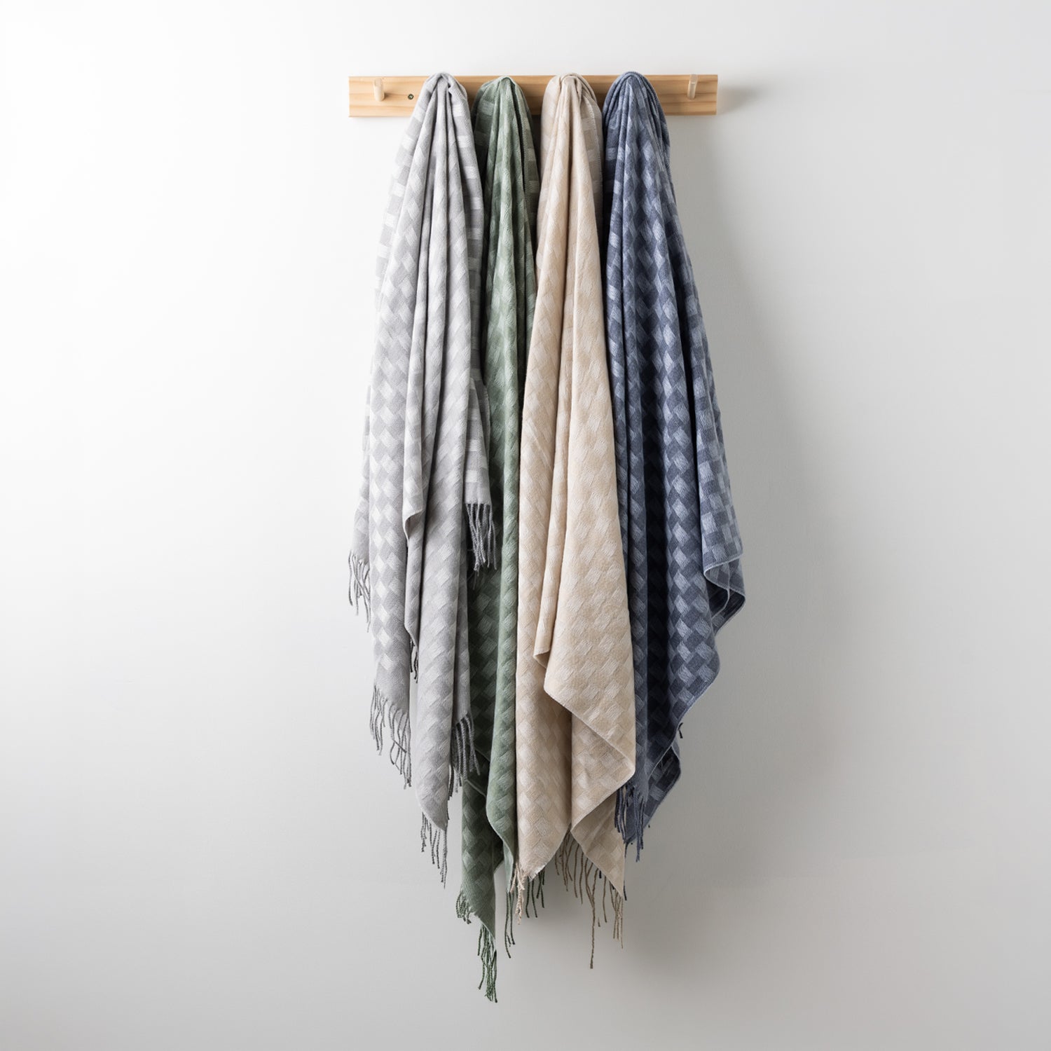 Home Co. Solane Check Throw range in Silver, Sage, Natural and Blue, displayed together on a wooden wall rack.