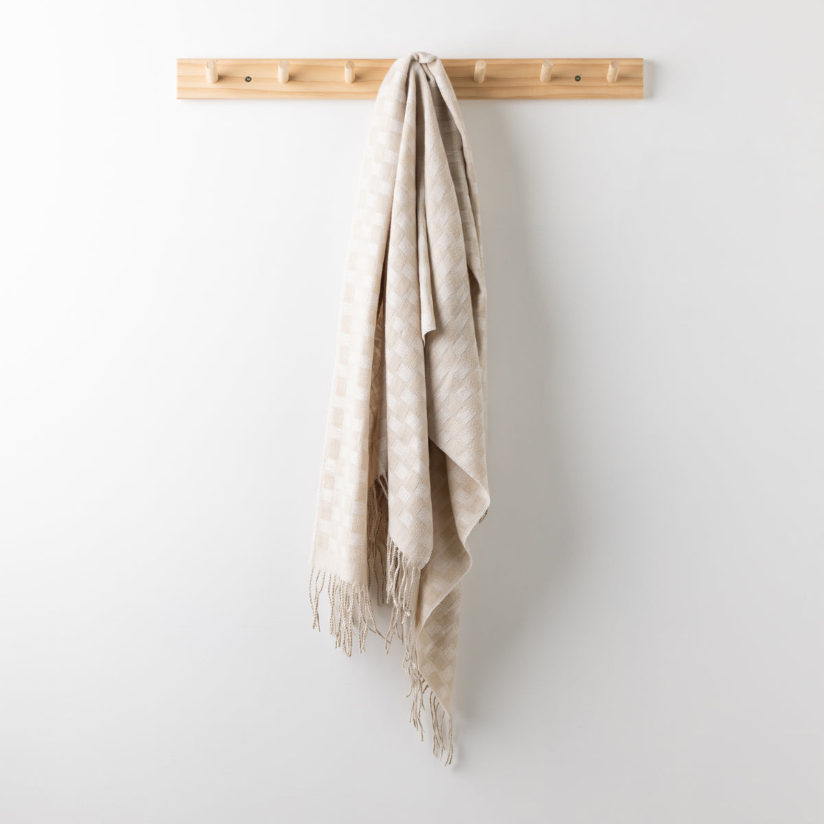 Home Co. Solane Check Throw in Natural featuring a soft tonal check pattern and fringed edges, hanging from a wooden wall rack.