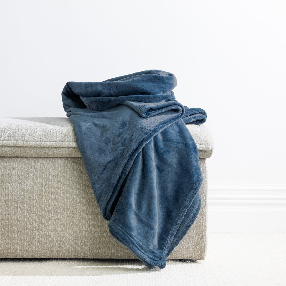 Blue: Home Co. Fraser Throw in blue, draped over a neutral upholstered ottoman in a bright interior.