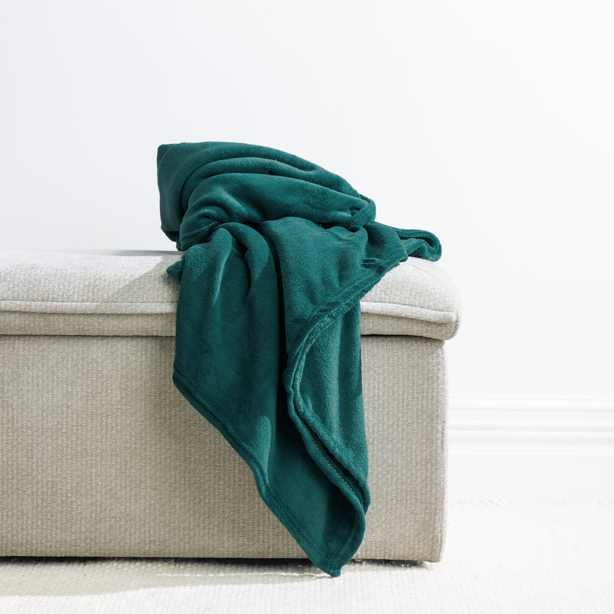 Green: Home Co. Fraser Throw in deep green, casually draped over a neutral upholstered ottoman.