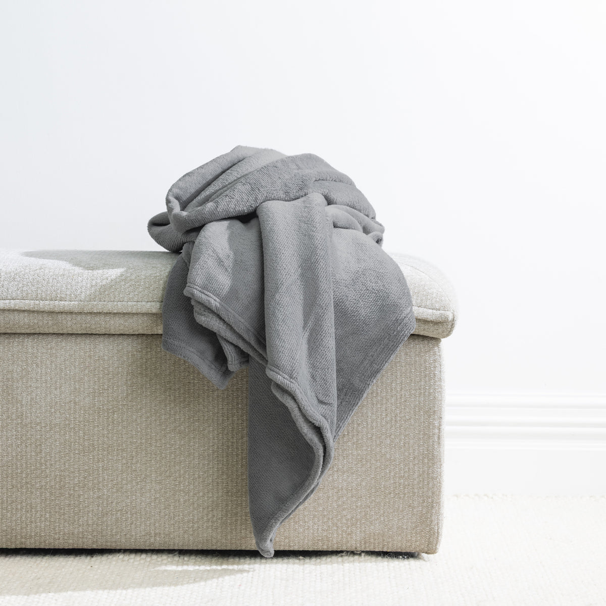 Grey: Home Co. Fraser Throw in grey, arranged over a neutral upholstered ottoman against a white background.