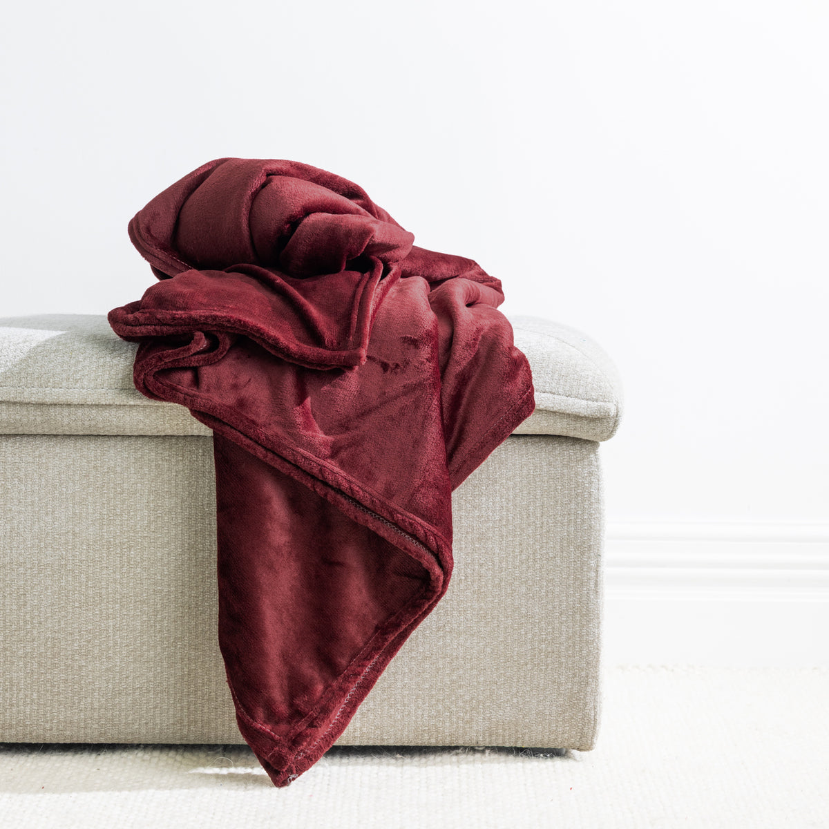 Wine: Home Co. Fraser Throw in deep wine red, arranged over a neutral upholstered ottoman against a bright white background.