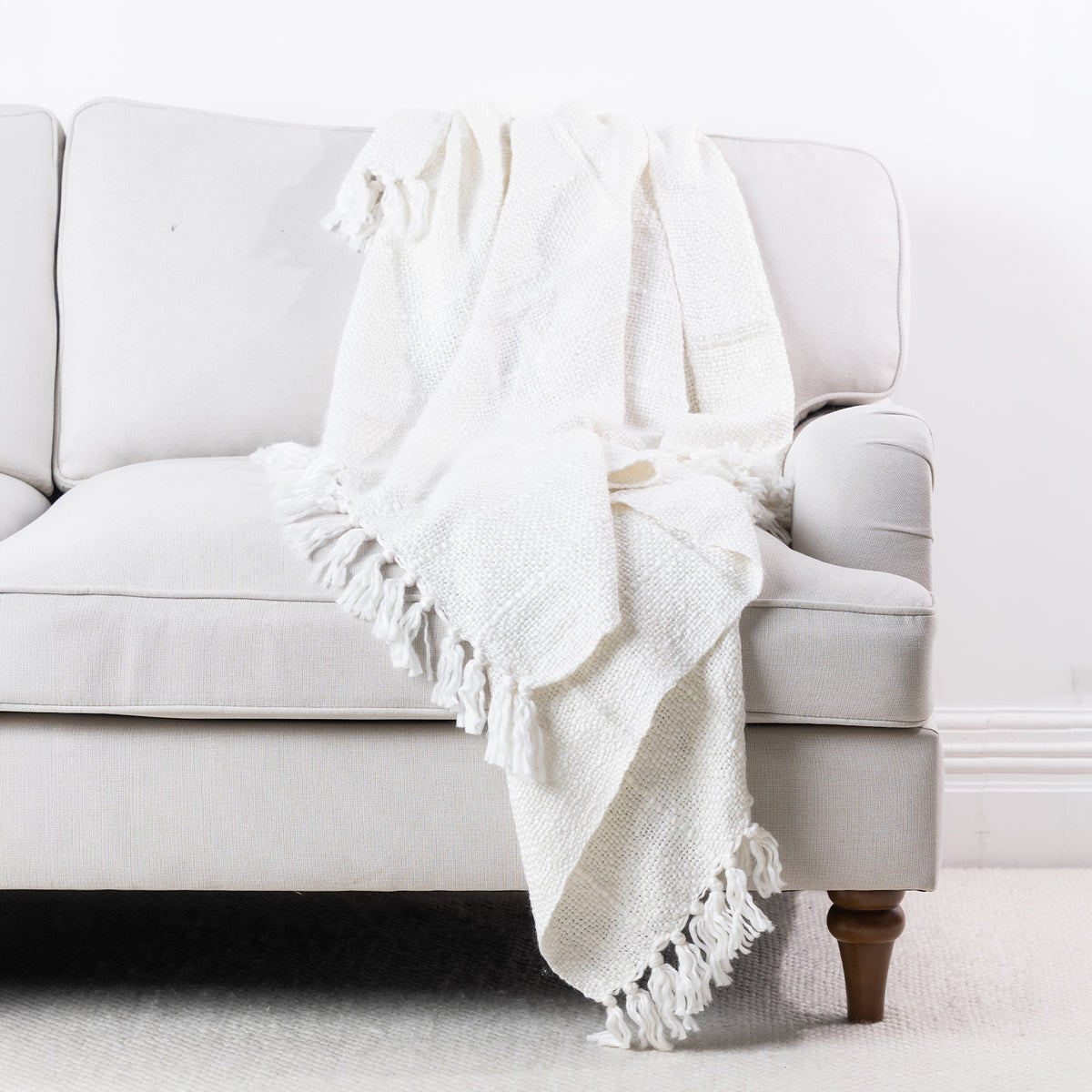 Ivory woven throw draped over a cream sofa, featuring a textured finish and fringed edges.